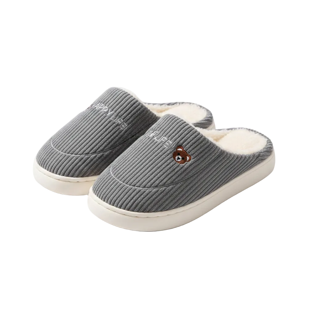 A pair of gray ribbed knit slip-on house slippers with white fleece lining, cream soles, embroidered text on one slipper, and a small embroidered bear face on the other, shown on a white background.