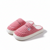 A pair of pink ribbed knit slip-on house slippers with white soles. One slipper features the text 'COZY LIFE' embroidered on the side, and the other has a small embroidered bunny face.