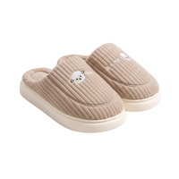 A pair of beige ribbed slip-on slippers with a small embroidered white bear face on the front and white lettering on the side, shown on a clean white background.