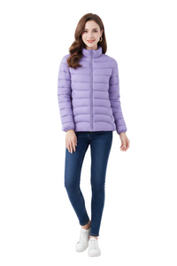 A woman modeling a light purple puffer jacket, paired with dark blue skinny jeans and white sneakers, against a plain white studio background.