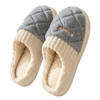 A pair of plush indoor slippers with a gray quilted upper and cream ribbed trim and lining, shown on a clean white background. A small brown brand patch on the side reads COMFY.