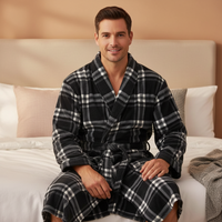 A man wearing a black and white plaid bathrobe sits on a bed in a bedroom setting.