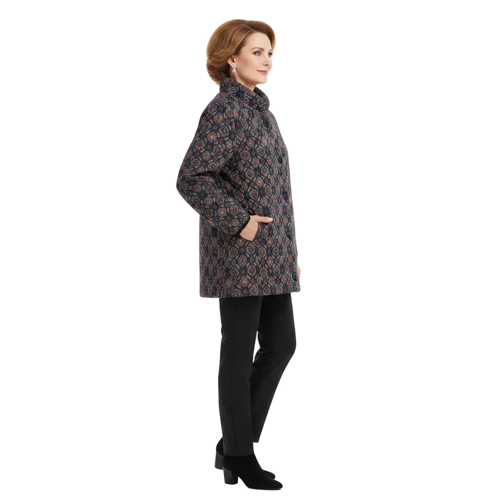 A woman modeling a mid-length quilted jacket with a geometric pattern in navy, rust orange, and beige, paired with black trousers and black ankle boots against a plain white background.