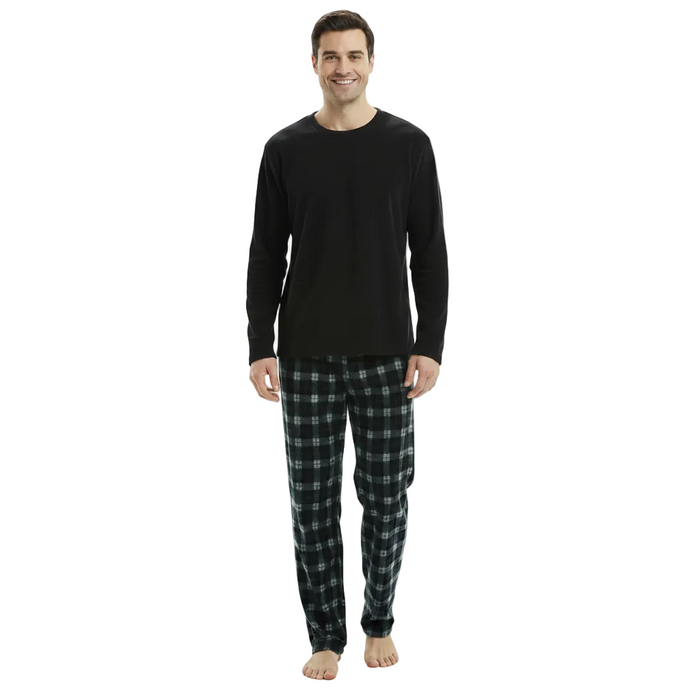 A man standing against a plain white background wearing a black long-sleeve shirt and dark green and black plaid pajama pants.