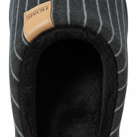 Close-up of a slip-on slipper showing the black pinstriped fabric exterior, plush black interior lining, and a tan leather brand tab with 'HOME' printed on it.