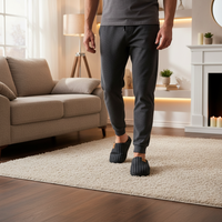 A man wearing dark gray lounge pants and matching slip-on slippers stands on a cream shag rug in a cozy living room with a beige sofa, floor lamp, and fireplace in the background.