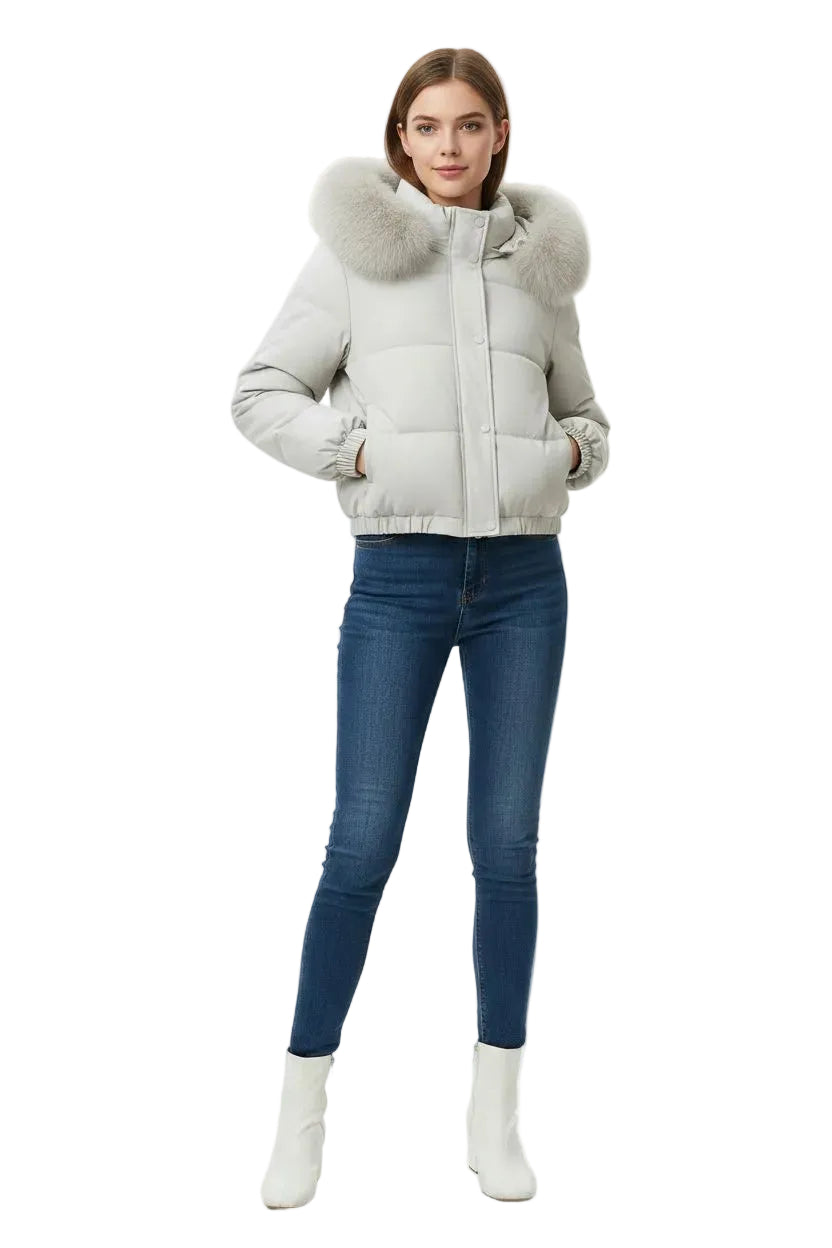 A woman modeling a light gray puffer jacket with a large fluffy faux-fur collar, paired with dark blue skinny jeans and white ankle boots, against a plain white studio background.