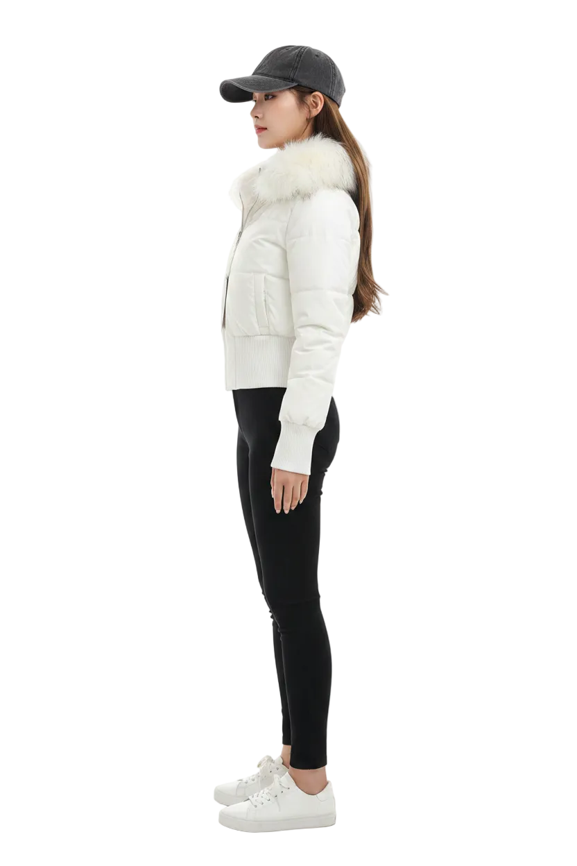 A woman in profile wearing a white puffer jacket with a fluffy light beige fur collar, black skinny pants, white sneakers, and a dark gray baseball cap, photographed against a seamless white studio background.