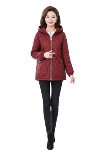 A woman modeling a quilted, cropped hooded jacket in a deep burgundy red. The jacket features a diamond-quilted pattern, a front zipper, and a hood.