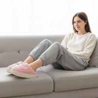 A woman sits on a light gray sofa wearing pink striped slip-on slippers with white soles, a cream sweatshirt, and light gray jogger pants.