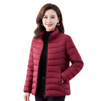 A woman wearing a short, quilted puffer jacket in a deep burgundy red over a black top, photographed against a solid white background.