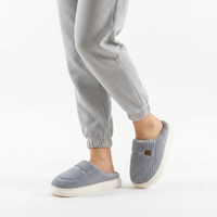 A person wearing light gray jogger pants and matching ribbed slip-on slippers with white soles, shown against a clean white studio background.