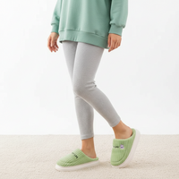 A person wearing light gray ribbed leggings and matching light green slip-on slippers, shown from the torso down against a clean white studio background.