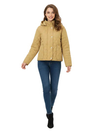 A woman modeling a tan quilted jacket with a high collar, paired with blue jeans and black ankle boots, against a plain white studio background.